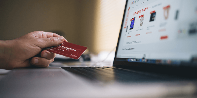 Someone holding a credit card in front of a laptop.