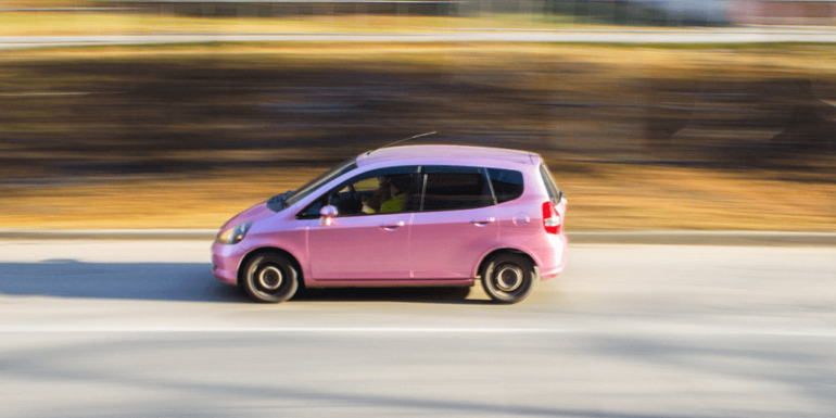 A pink car speeding along a highway.